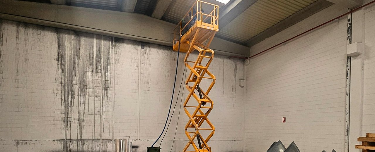 Plataforma elevadora en nave industrial con hollín por incendio — limpieza en altura